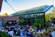 a group of people sitting in front of a green house with lots of plants and trees