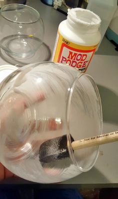 a person holding a paintbrush in front of a glass cup with liquid inside it