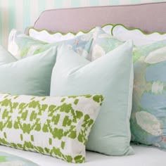 a bed topped with lots of pillows next to a green headboard and foot board