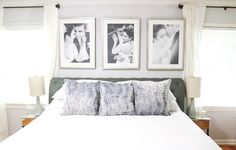 a white bed topped with pillows next to two pictures on the wall above it's headboard