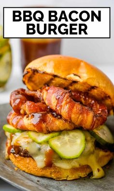 a bacon burger on a bun with pickles and cucumbers in the foreground