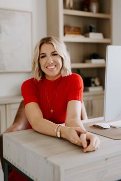 a woman sitting at a desk in front of a computer monitor smiling for the camera