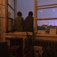 two people are sitting on a window sill looking out at the city below them