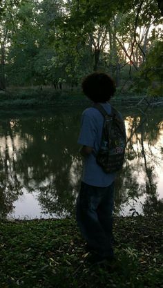 a person with a backpack standing by the water in the woods looking at the trees