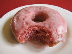 a glazed doughnut with pink icing on a white plate and red tablecloth