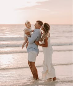 a man and woman holding a baby on the beach at sunset with waves coming in