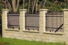 a stone wall with wrought iron fencing on the top and bottom, in front of a tree