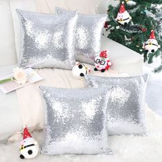 three silver sequin pillows sitting on top of a white couch next to a christmas tree