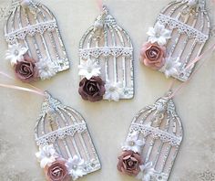 four birdcages decorated with flowers and ribbons on a white tablecloth, next to a pink rose