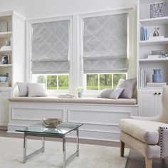 a living room filled with white furniture and windows covered in roman blind shades on the windowsill