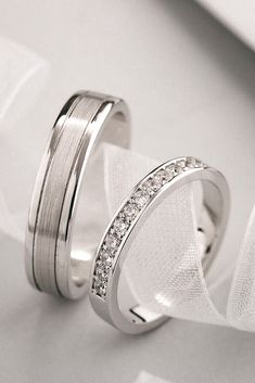 two white gold wedding rings with diamonds on them, sitting next to each other in front of a cloth