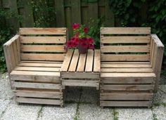 two wooden benches sitting next to each other on top of a gravel ground with flowers in the background