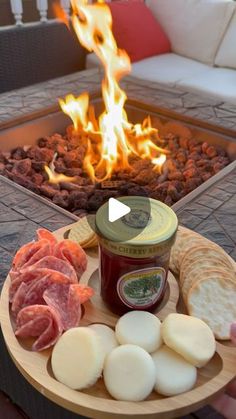 a person holding a plate with meats and cheeses on it in front of a fire pit