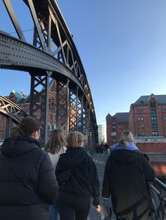 three people walking on a bridge with buildings in the background