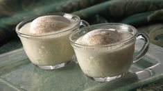 two glasses filled with dessert sitting on top of a glass table