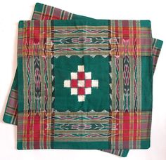 a green and red blanket with a cross on the front, sitting on a white surface