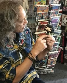 a man sitting in front of a display of comic books holding a doll and looking at it