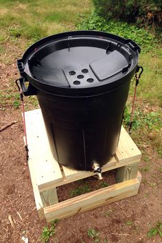 a large black trash can sitting on top of a wooden pallet in the grass