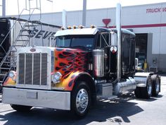 a large semi truck with flames painted on it's front and sides parked in front of a building