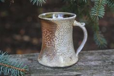 a mug sitting on top of a wooden table next to a pine tree and needles