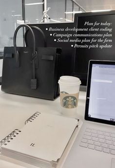 a laptop computer sitting on top of a desk next to a purse and coffee cup