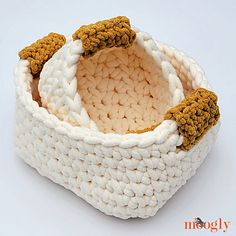 a crocheted white basket with two brown pom - poms