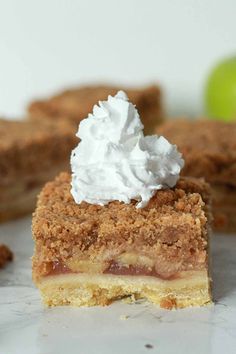 a piece of pie with whipped cream on top and an apple in the back ground