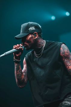 a man with tattoos on his arm holding a microphone to his mouth and wearing a black hat