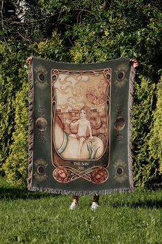 a woman holding up a tapestry in the grass