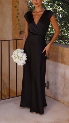 a woman in a black dress standing next to a plant and holding a white bouquet