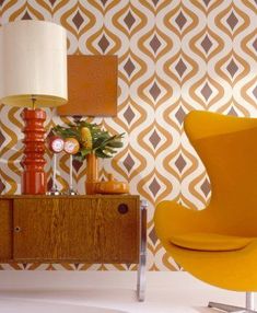 an orange chair sitting next to a lamp on top of a wooden table in front of a wall