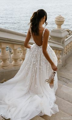 a woman in a white dress is walking down some stairs by the water and looking at something