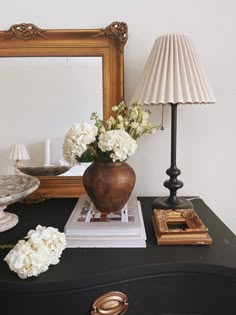 a vase with white flowers sitting on top of a black dresser next to a mirror