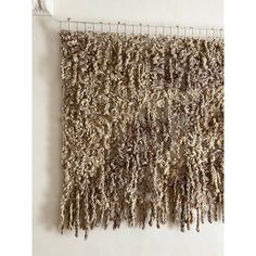 a wall hanging on the side of a white wall next to a metal rack filled with yarn