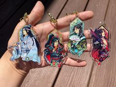 four anime keychains in the palm of someone's hand on a wooden deck