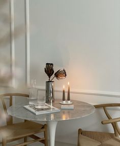 a table with two candles on it in front of a white wall and some chairs