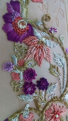 an embroidered piece with flowers and leaves on it's side, sitting on a table