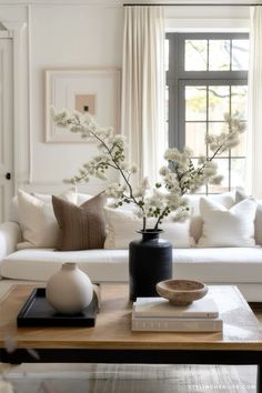 a living room filled with white furniture and flowers on top of a wooden coffee table