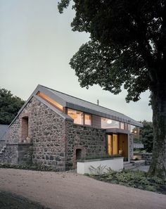 a stone house with a tree in the foreground and another building on the other side