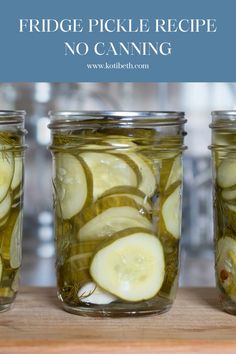 three jars filled with pickles sitting on top of a wooden table next to each other