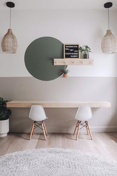 two white chairs sitting under a wooden table in front of a green circle on the wall