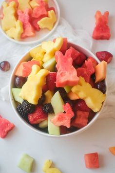 two bowls filled with cut up fruit on top of a white table next to each other