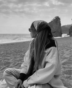 a woman sitting on top of a sandy beach next to the ocean