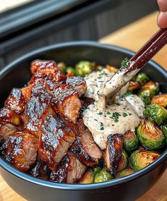 someone is holding chopsticks over a bowl of meat and brussel sprouts