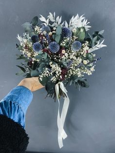 a person holding a bouquet of flowers with white and blue flowers on it's side