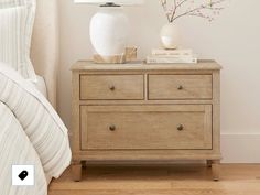 a white vase sitting on top of a wooden dresser next to a lamp and bed