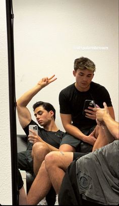 two men sitting on a couch in front of a mirror with their cell phones up