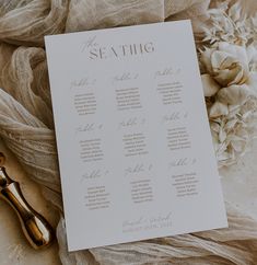 a table plan sitting on top of a white cloth next to a gold vase filled with flowers