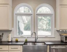 a kitchen with white cabinets and black counter tops next to two large windows that have double panes over them