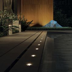 an empty swimming pool at night with lights shining on the water and plants growing around it